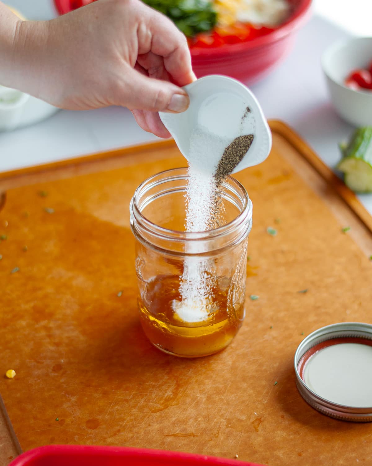 Process shot showing the salt and pepper being added to a jar with the rest of the ingredients for the dressing.