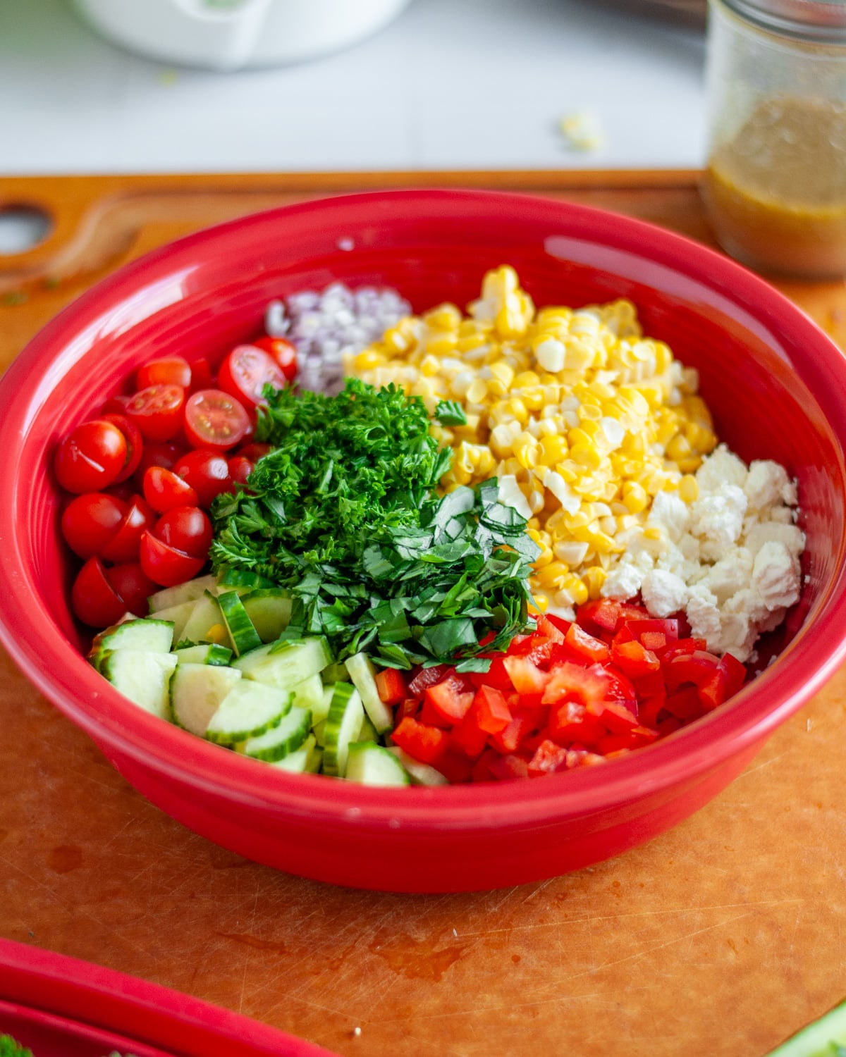Process shot showing all of the chopped salad ingredients in a large red bowl.