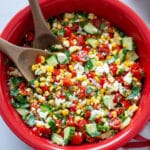 Close up of the summer corn salad in a large red bowl with wooden salad spoons.