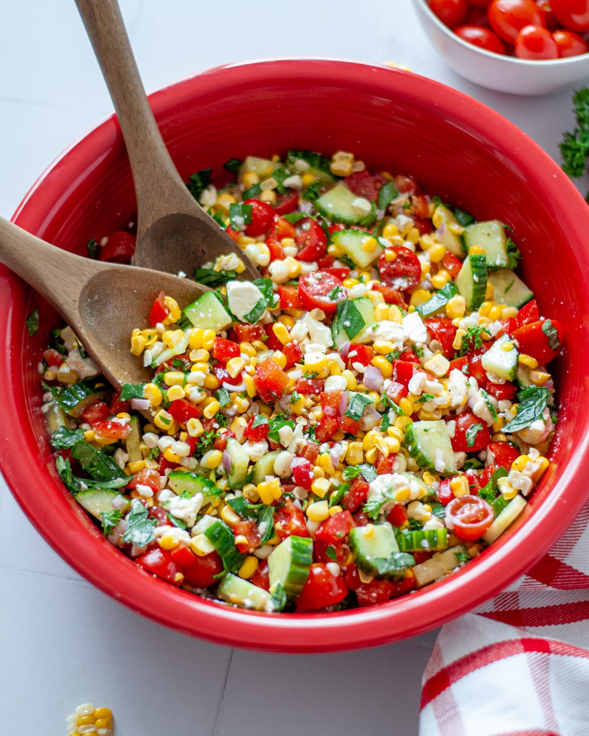 Close up of the summer corn salad in a large red bowl with wooden salad spoons.