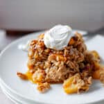A scoop of peach baked oatmeal topped with maple syrup and a dollop of vanilla greek yogurt on a white serving plate.