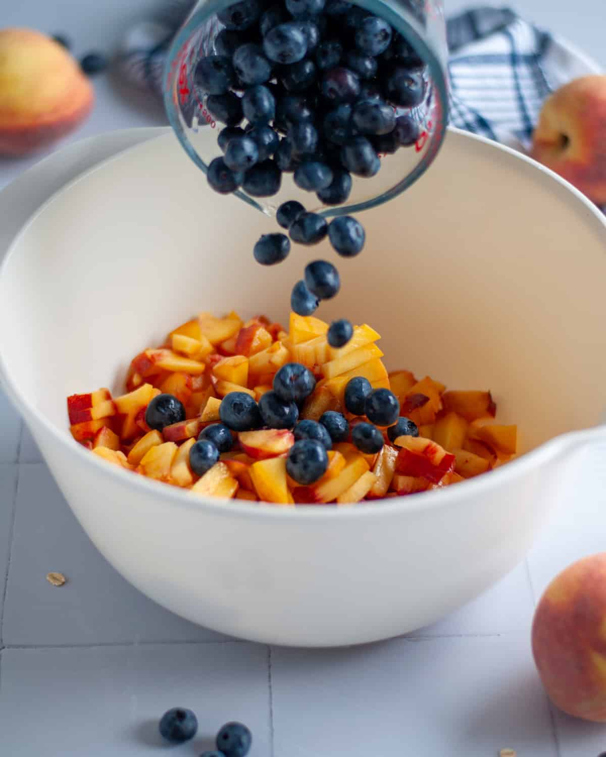 Process shot showing the blueberries being added into a large mixing bowl with the chopped peaches.