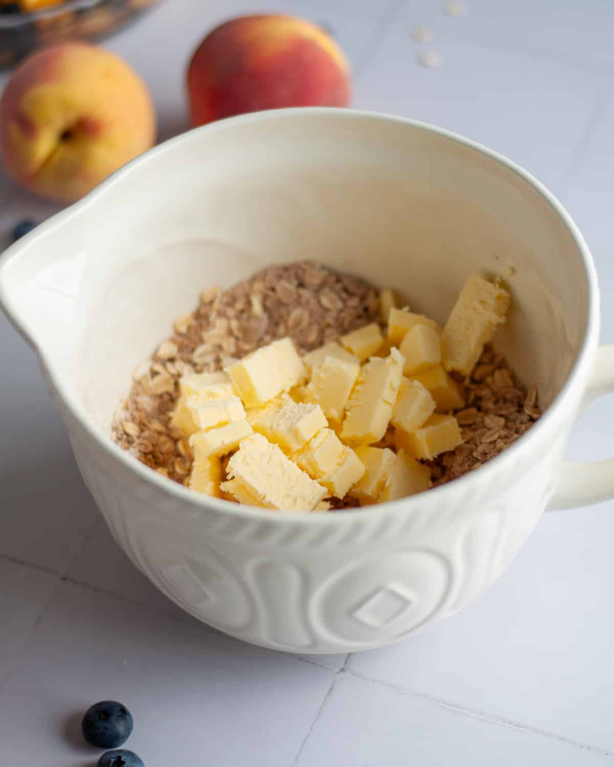 Process shot showing the cold, cubed butter added into the mixing bowl with the other oat topping ingredients.