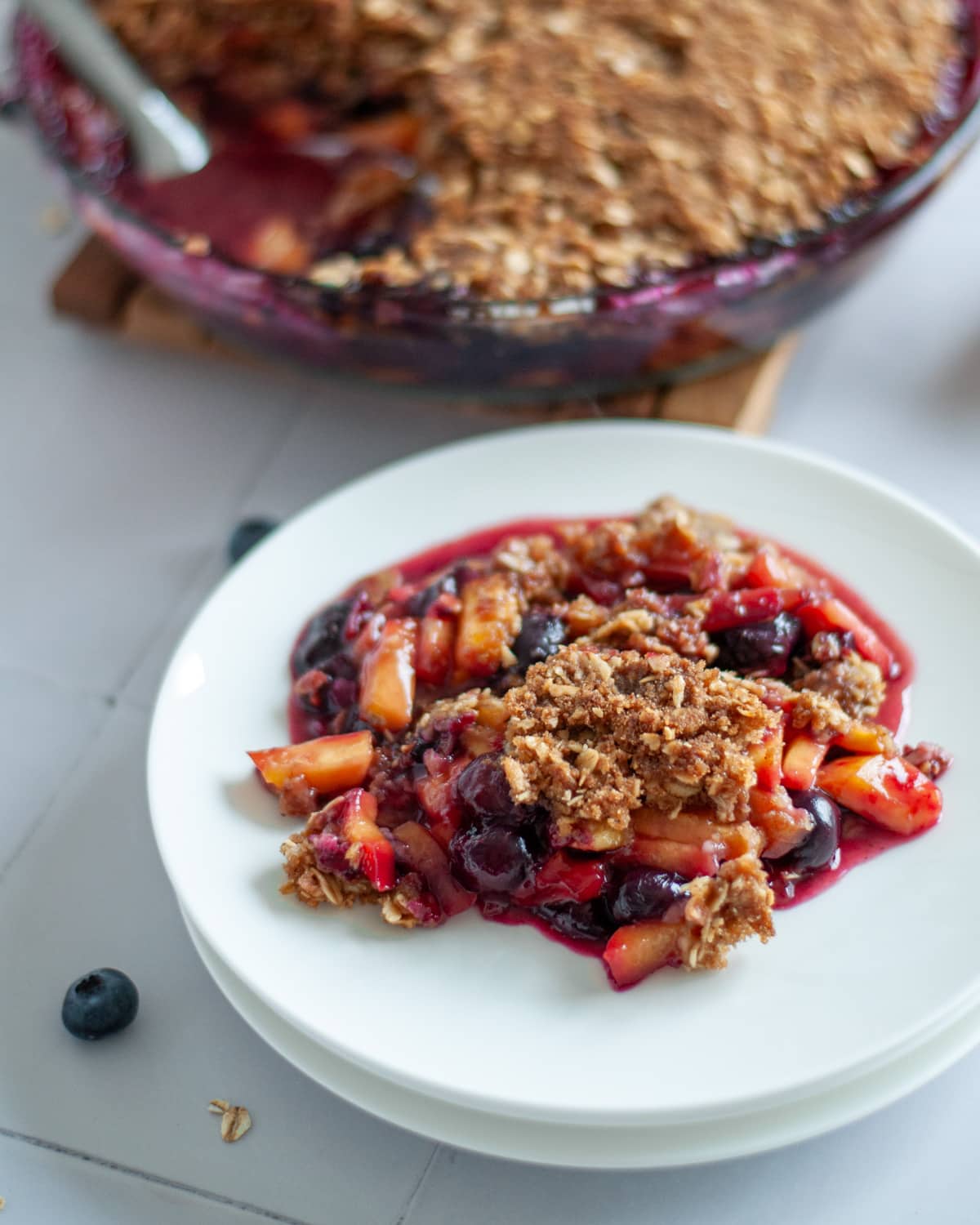 A scoop of peach and blueberry crisp on a white serving plate.