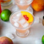 Two glasses of peach daiquiris, garnished with fresh peach slices, surrounded by iced and the other ingredients.