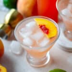 Two glasses of peach daiquiris, garnished with fresh peach slices, surrounded by iced and the other ingredients.