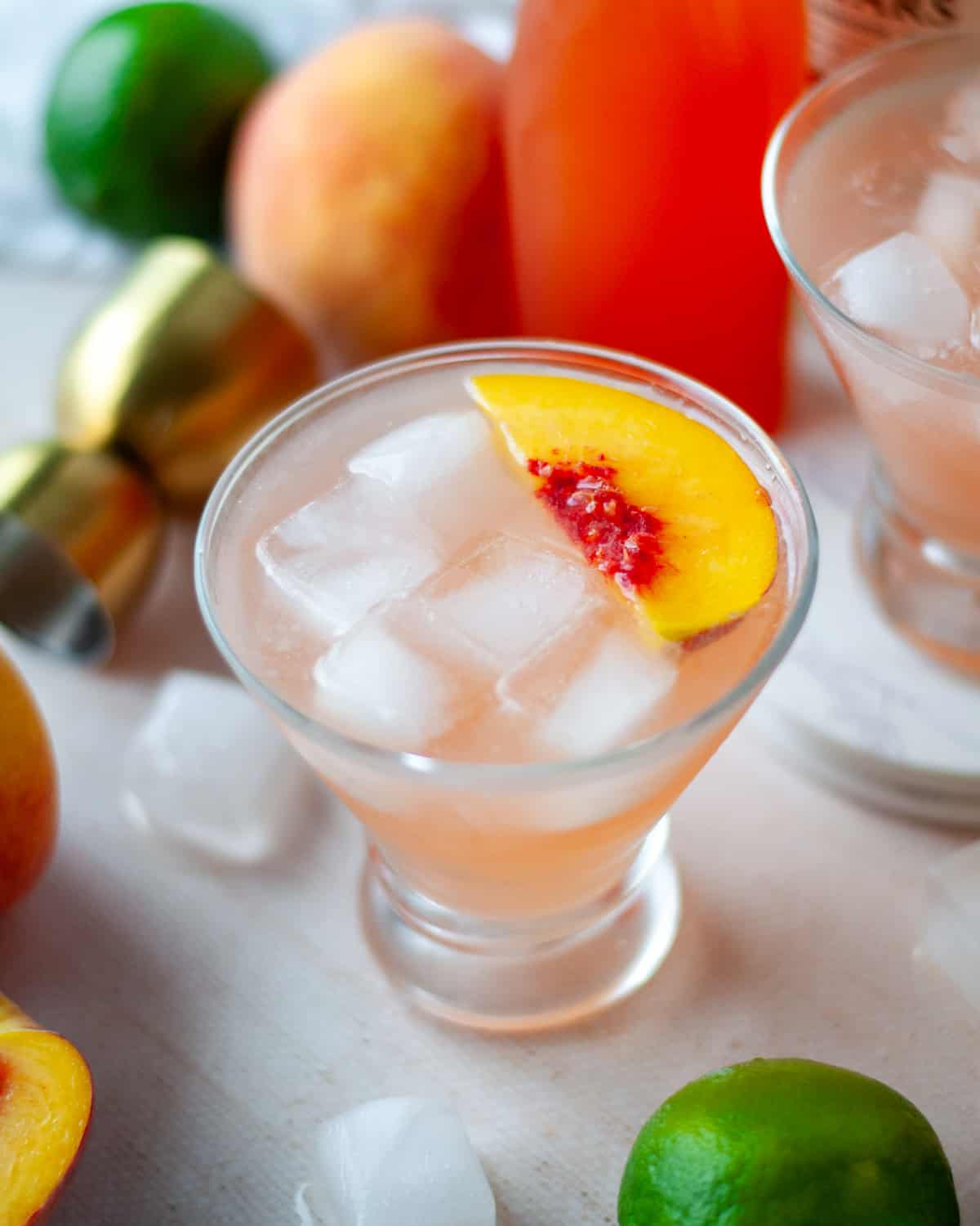 Two glasses of peach daiquiris, garnished with fresh peach slices, surrounded by iced and the other ingredients.