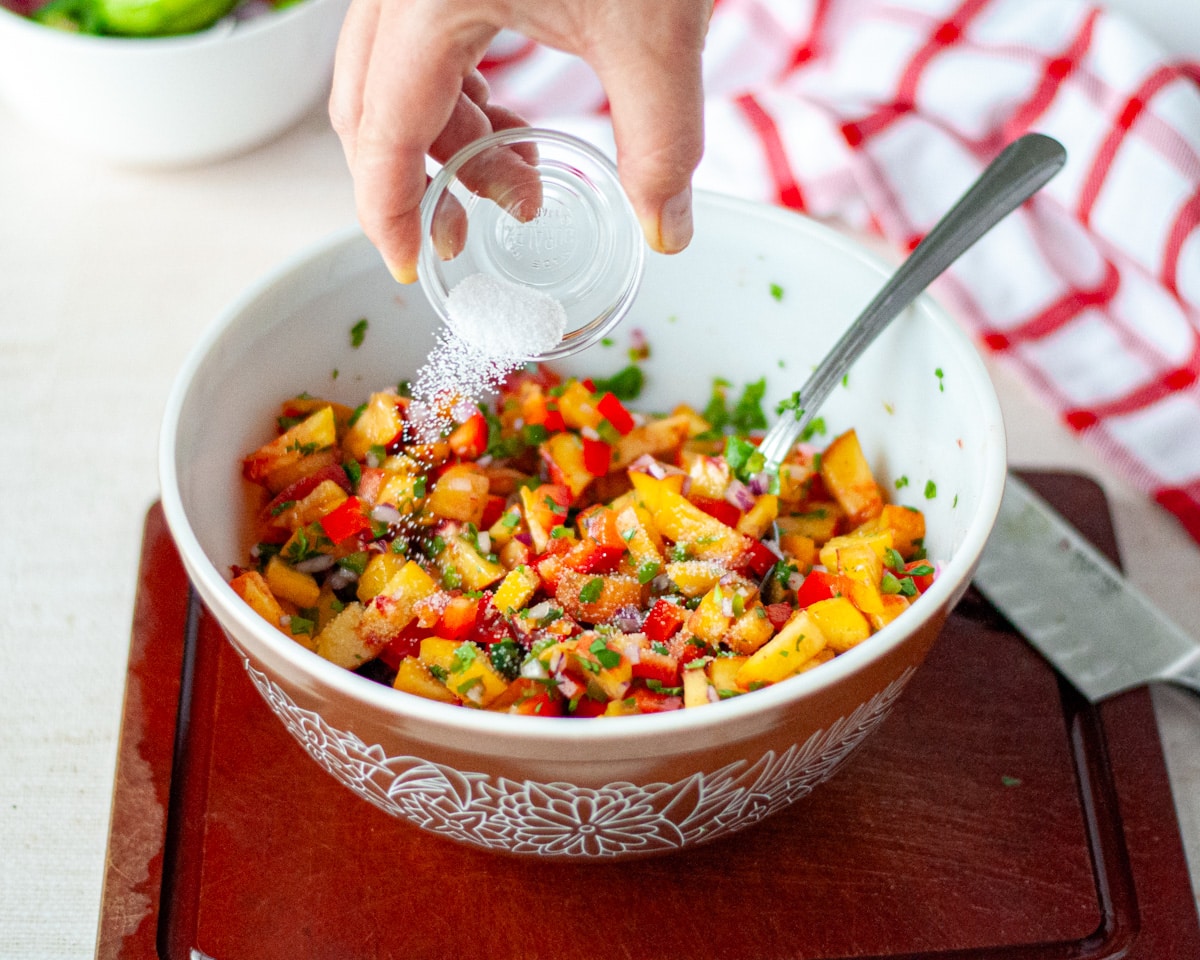 Process shot showing the salt being added to the peach salsa.