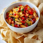 A bowl of peach salsa on a serving tray with tortilla chips.