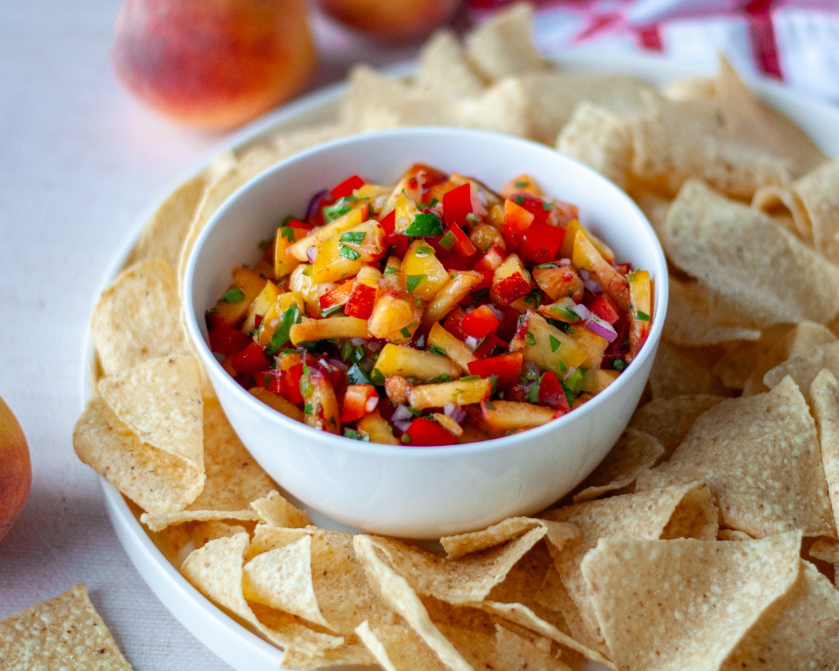 A bowl of peach salsa on a serving tray with tortilla chips.