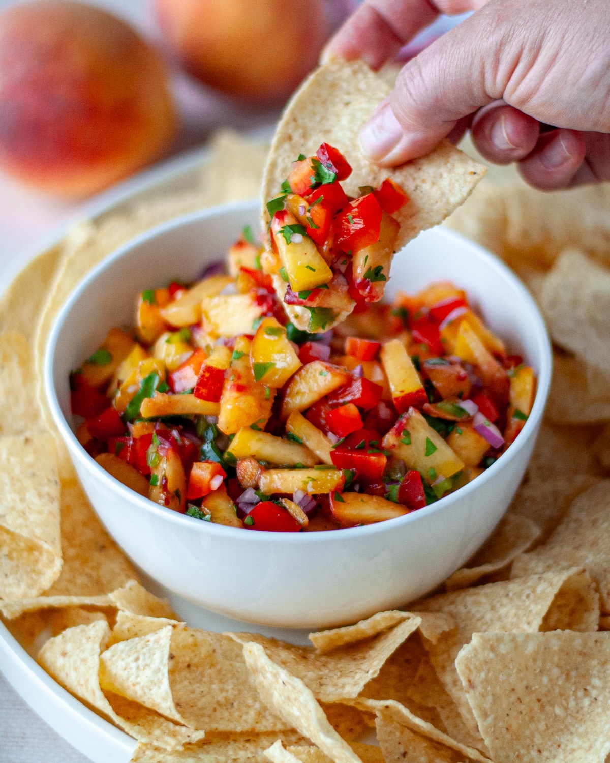 A hand with a tortilla chip dunked into the peach salsa, ready to eat it.
