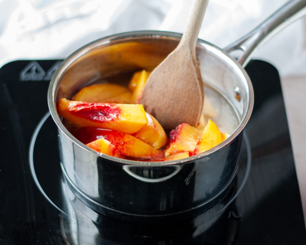 Process shot showing all of the peach syrup ingredients added to a small pan on the stove.