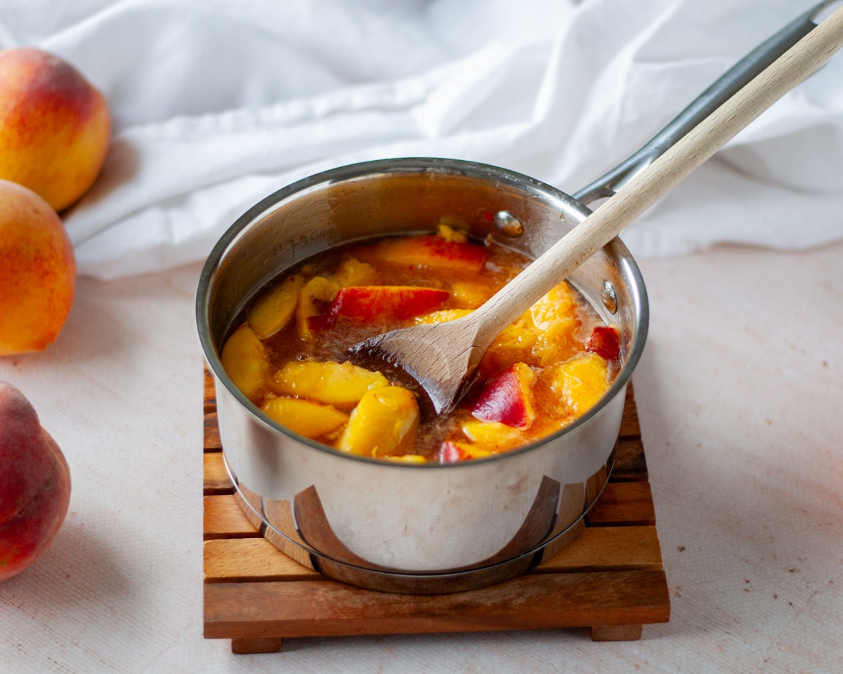 Process shot showing peach syrup resting, allowing the peaches to steep in the hot syrup.