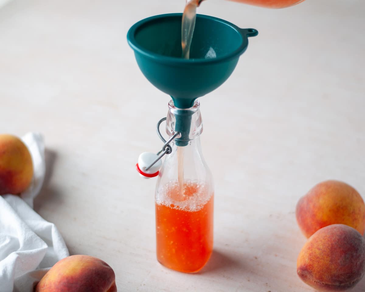Process shot showing the peach syrup being transferred to an airtight container with a funnel.