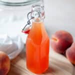 Close up of a glass bottle filled with peach syrup.
