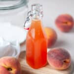 Close up of a glass bottle filled with peach syrup.