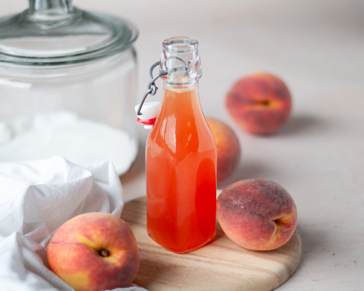 Close up of a glass bottle filled with peach syrup.
