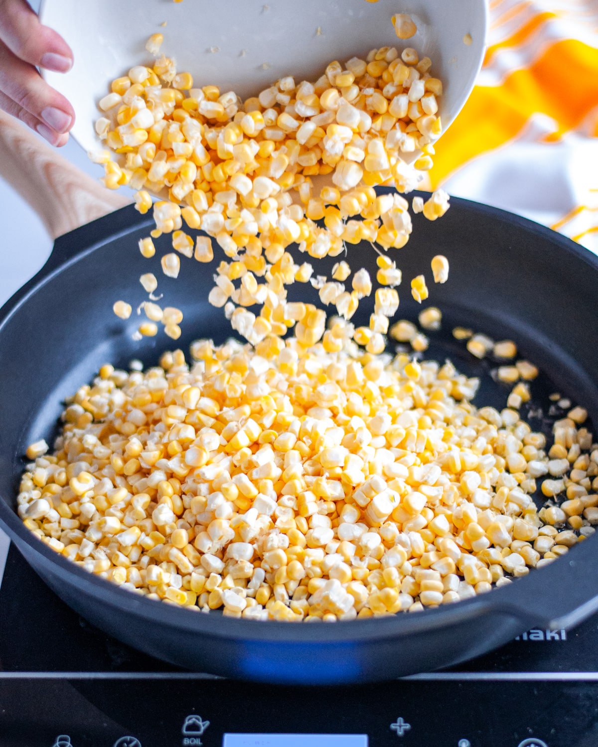 Process shot showing the raw corn kernels being added to the skillet with hot oil.