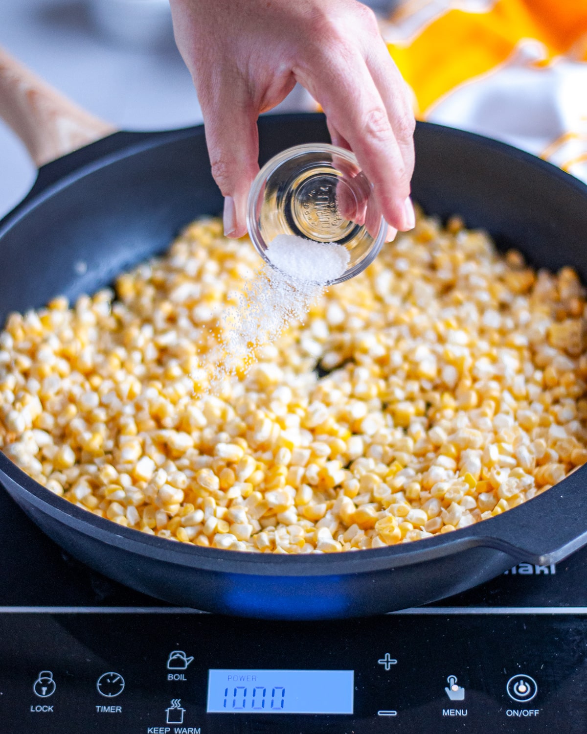 Process shot showing the salt being sprinkled over the corn kernels.