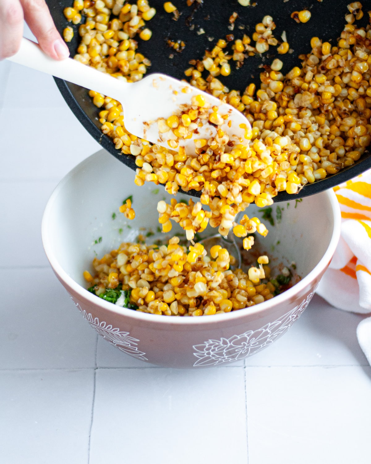 Process shot showing the cooked corn being added into the mixing bowl with the dressing and other corn salad ingredients.