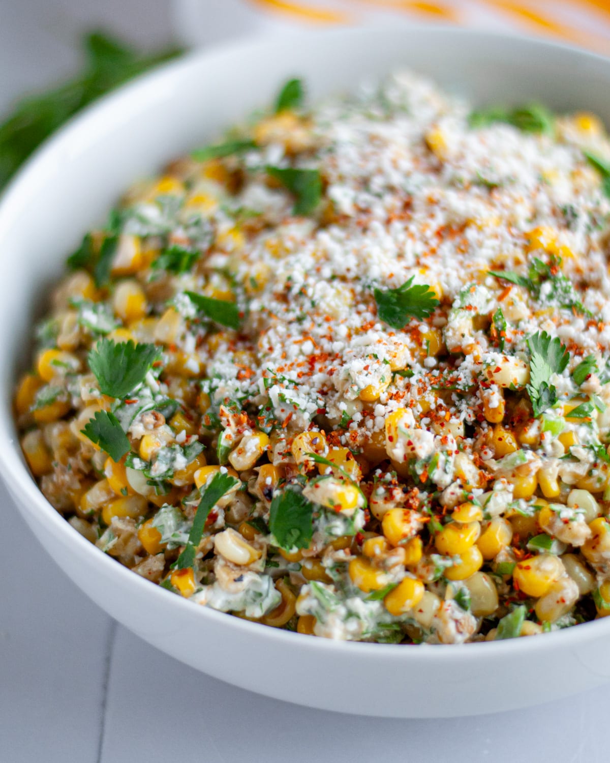 Close up of our Mexican street corn salad in a white serving bowl, topped with extra cotija cheese, tajin, and cilantro.