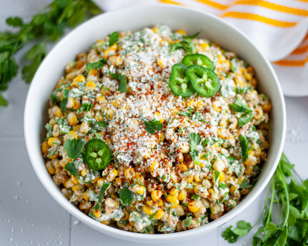 A serving bowl of Mexican street corn salad topped with extra cotija cheese, tajin, jalapeño slices, and cilantro.