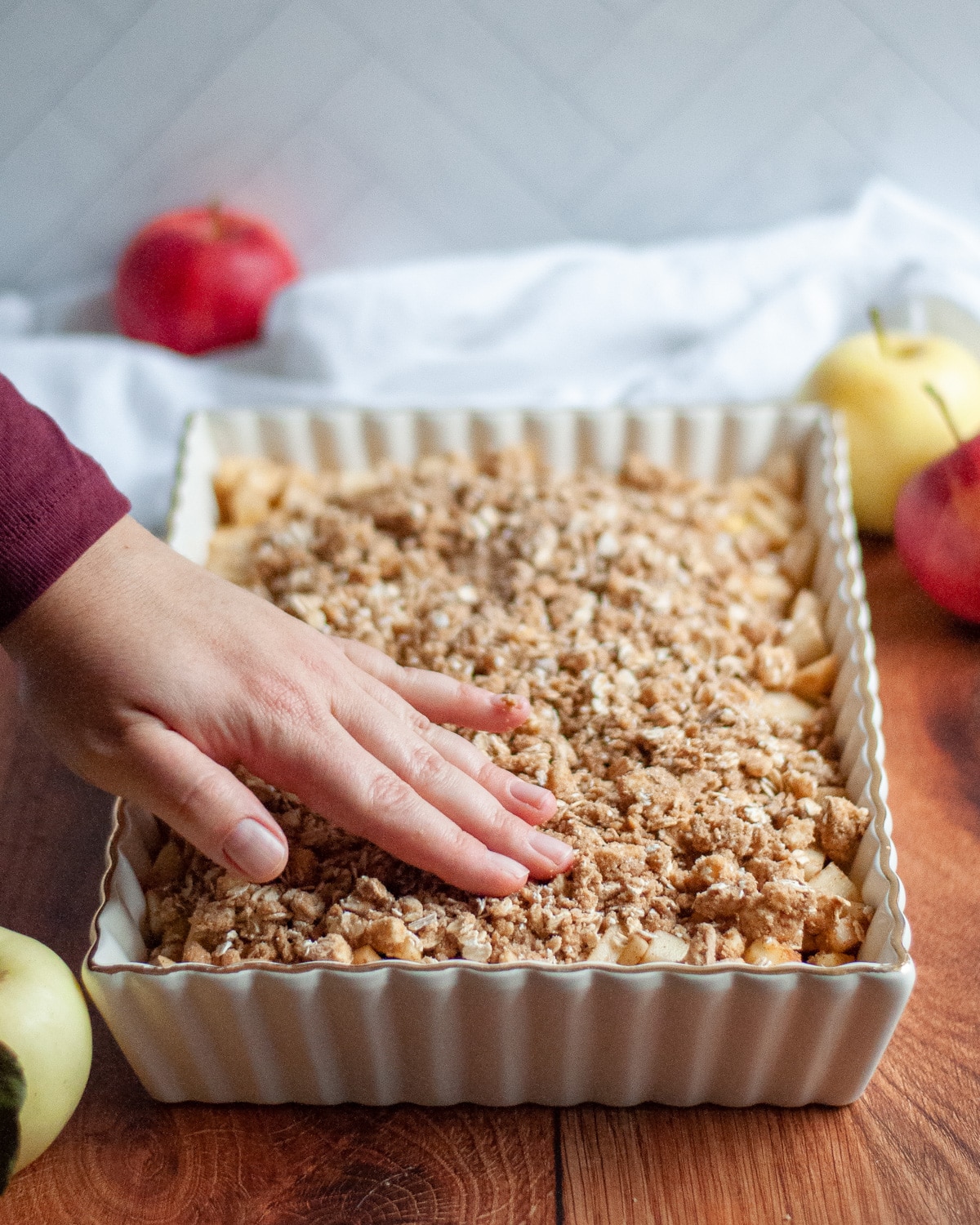 Process shot showing the oat topping being spread over the apple filling in the 9x13 pan.