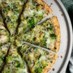 Close up of broccoli pizza sliced on a pizza pan.