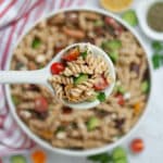 Top down shot of vegetarian Mediterranean Pasta Salad in a white serving bowl with a spoonful held up closer to the camera.