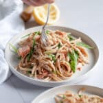 Close up of a white plate filled high with smoked salmon pasta, with a fork twirling a big bite of pasta.