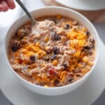 A bowl of white chicken chili with a hand taking a spoonful of chili to eat.