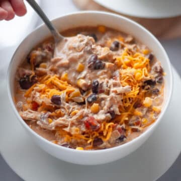 A bowl of white chicken chili with a hand taking a spoonful of chili to eat.