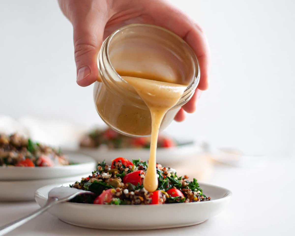 Pour shot of the maple tahini dressing going onto a plate filled with this power salad recipe.