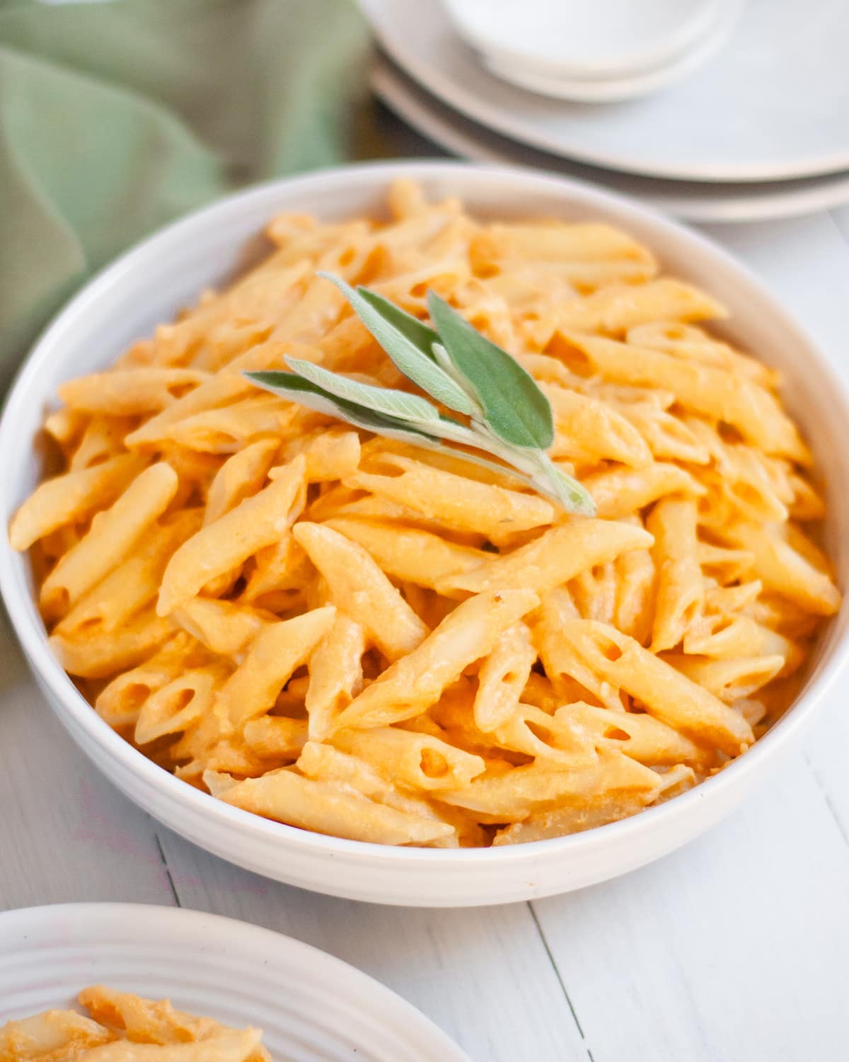 Serving bowl filled with pumpkin pasta with and boursin cheese garnished fresh sage on top.