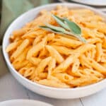 Serving bowl filled with pumpkin pasta with and boursin cheese garnished fresh sage on top.