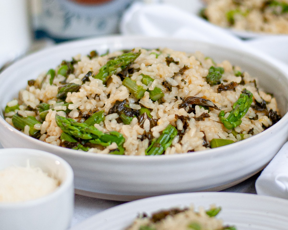 Close-up view of a white bowl of Summer Vegetable Risotto with asparagus and kale.