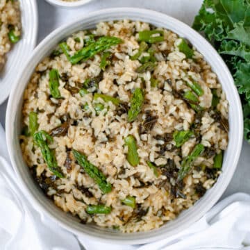 Top-down view of a white bowl of Summer Vegetable Risotto with asparagus and kale.