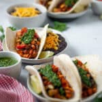 Three plates tacos, each served topped with homemade chimichurri sauce and a side of refried beans with cheese.