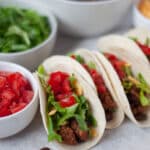 A tray of ground turkey and black bean tacos served in flour tortillas with lettuce, cheese, and diced tomatoes.