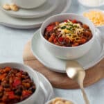 Three bowls of vegetarian chili surrounded by crackers, cheese, and sour cream for topping.