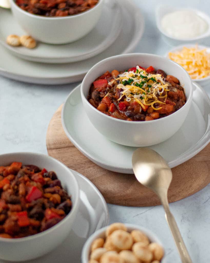 Three bowls of vegetarian chili surrounded by crackers, cheese, and sour cream for topping.
