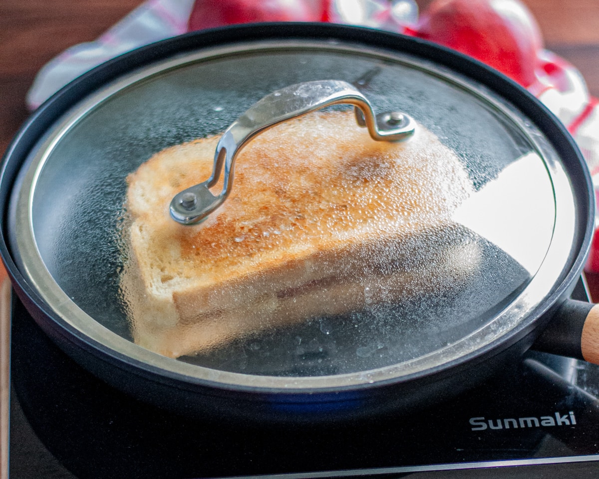 Process shot showing the apple grilled cheese cooking in the skillet with a cover over it to help the cheese melt.