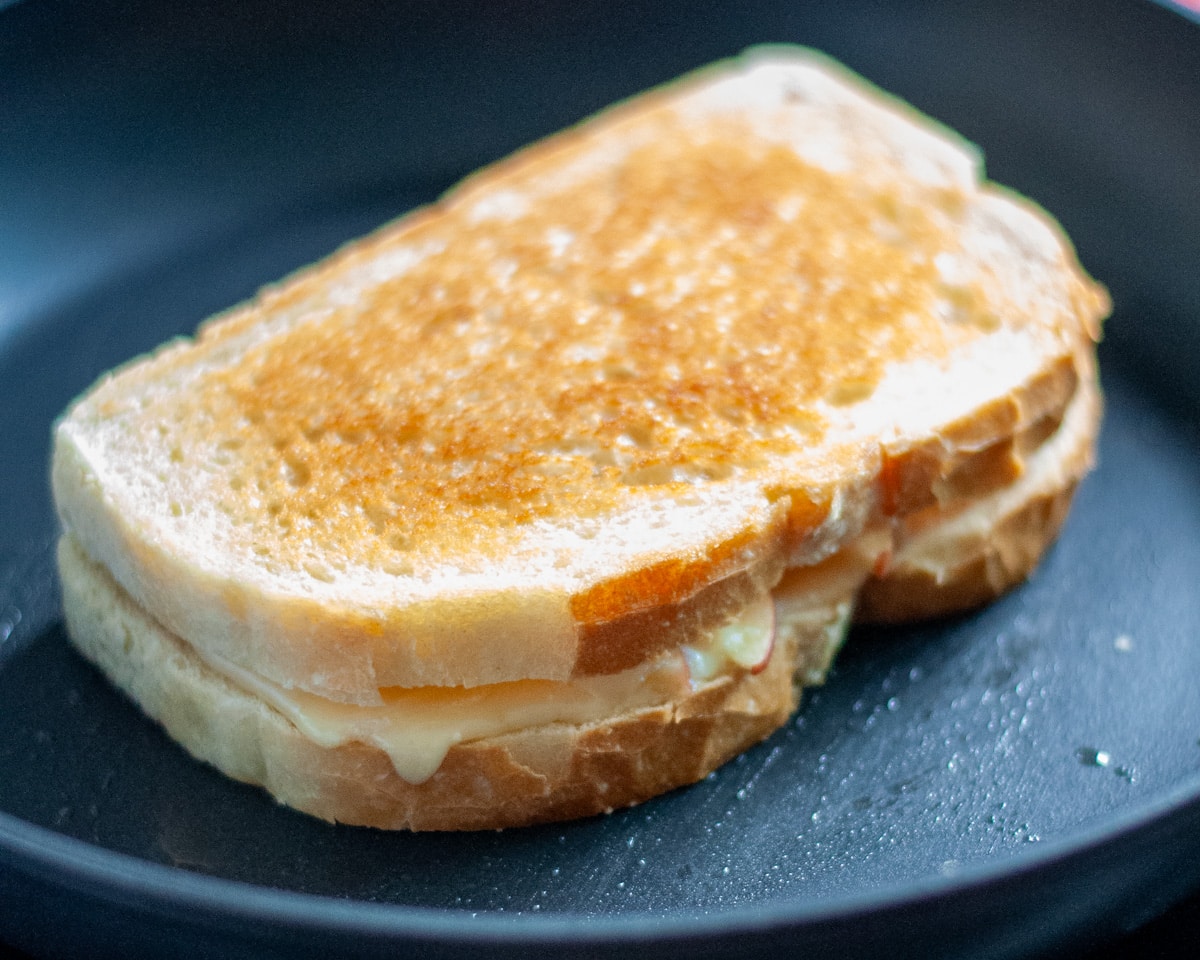 Process shot of the grilled cheese in the skillet showing the golden brown of the 1st side while the 2nd slice of bread cooks.