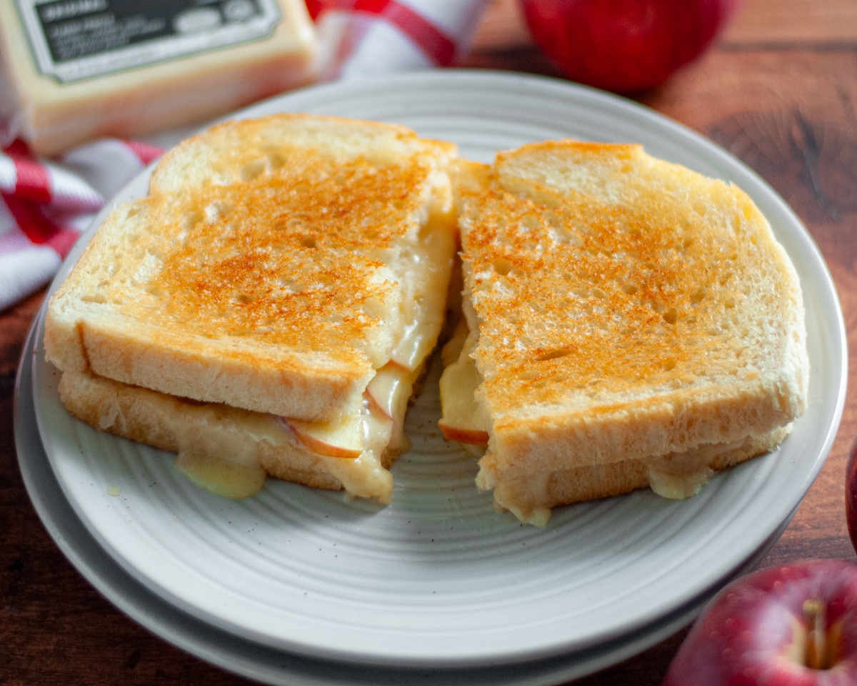 Close up of an apple grilled cheese sandwich sliced in half on a serving plate.