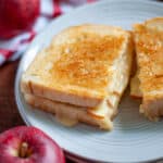 Close up of an apple grilled cheese sandwich sliced in half on a serving plate.