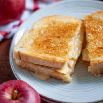 Close up of an apple grilled cheese sandwich sliced in half on a serving plate.