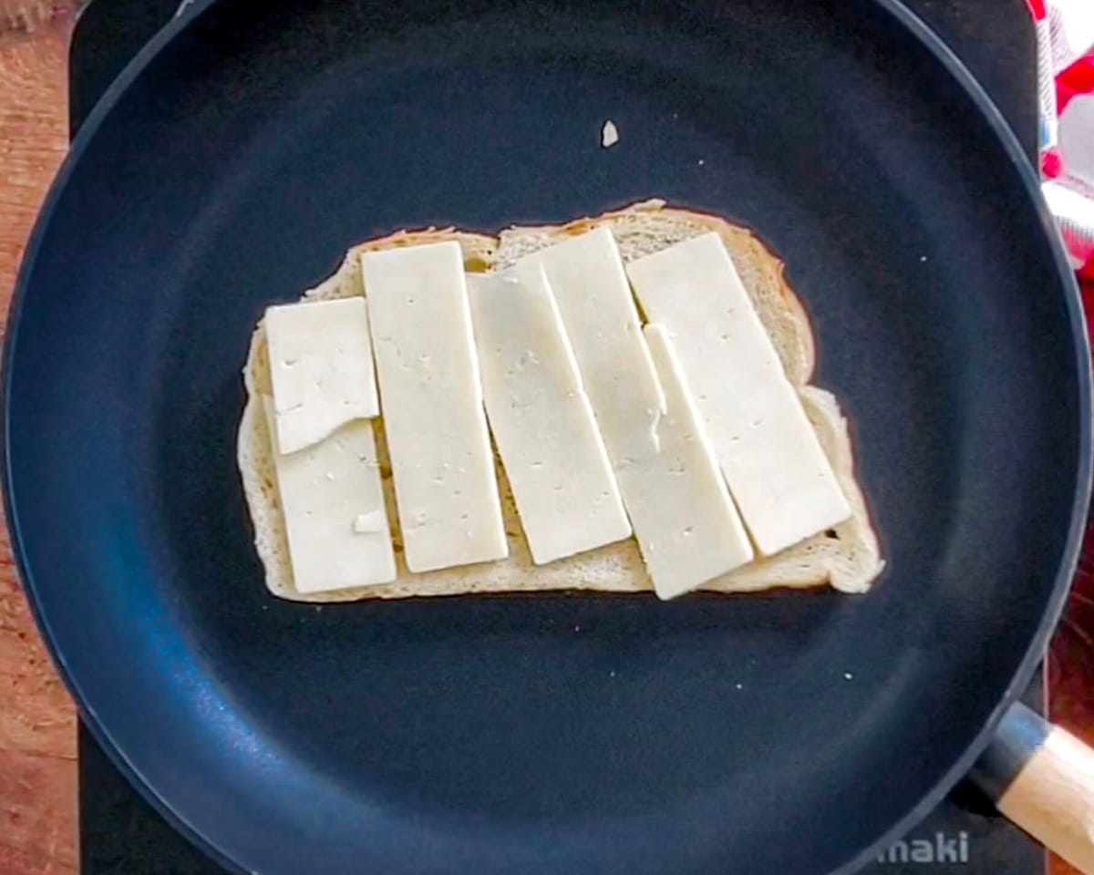 Process shot showing one slice of bread butter side down in the skillet with a layer of cheese slices.