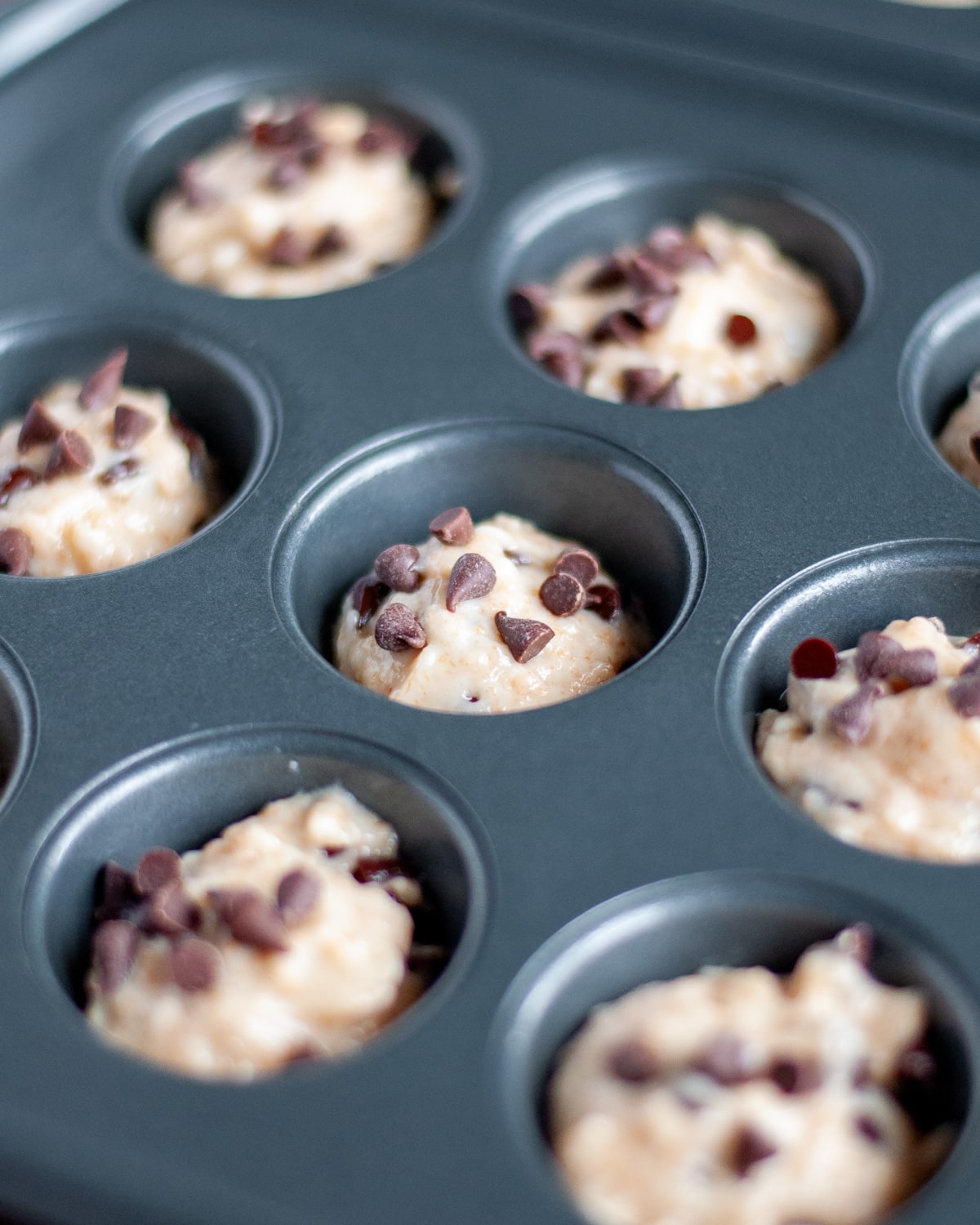 Close up of the mini chocolate chip muffin batter in the prepared muffin tins with extra mini chocolate chips added on top.
