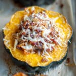 Close up of a baked stuffed acorn squash with sausage and apples on a parchment lined baking sheet.