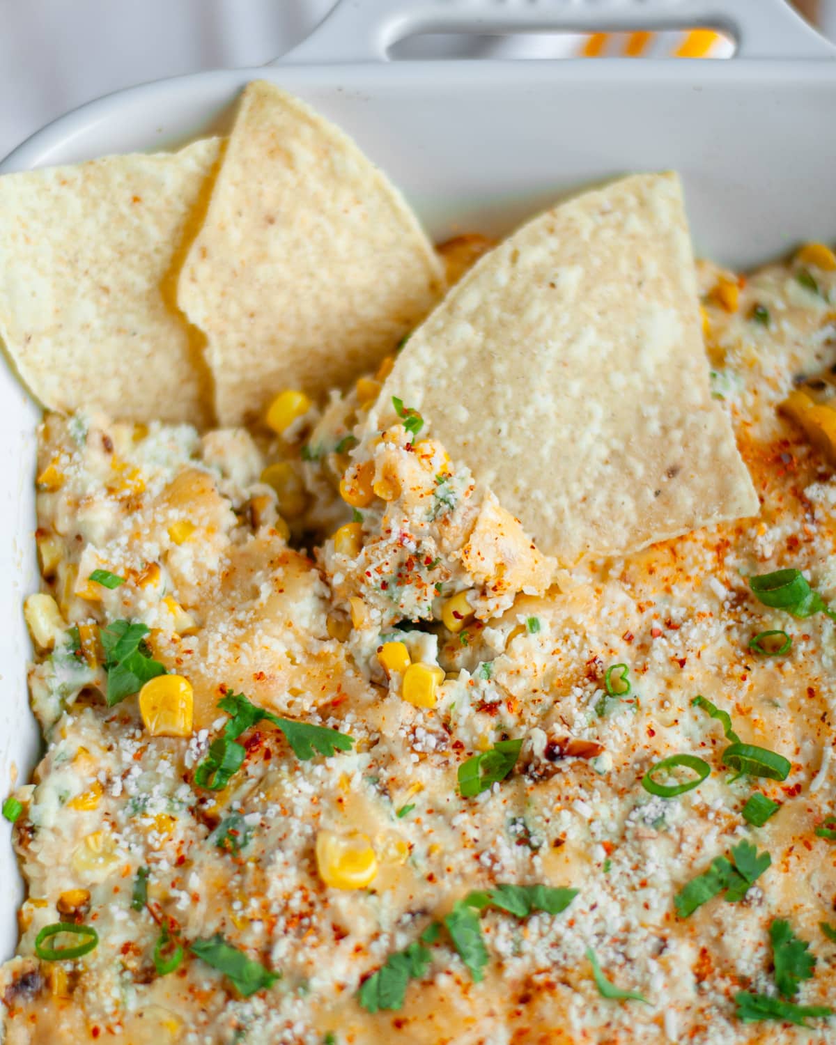 Close up of three chips dunked into a white baking dish of Mexican street corn dip.